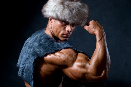 Strong athletic man in a fur cap isolated over black backgroundの写真素材
