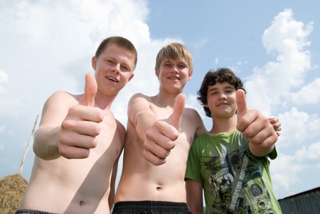 Three cheerful boys show thumbs against the skyの写真素材