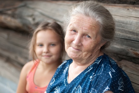 The elderly woman with the grand daughter against the wooden houseの写真素材