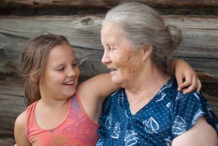 The elderly woman with the grand daughter against the wooden houseの写真素材