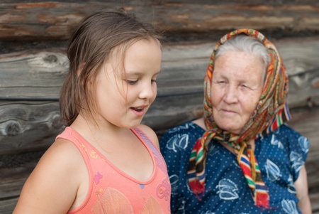 The elderly woman with the grand daughter against the wooden houseの写真素材