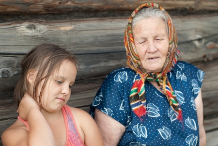 The elderly woman with the grand daughter against the wooden houseの写真素材