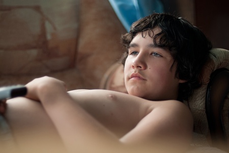 The boy lies on a sofa and watches TVの写真素材