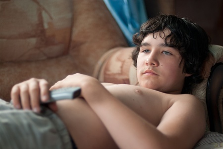 The boy lies on a sofa and watches TVの写真素材