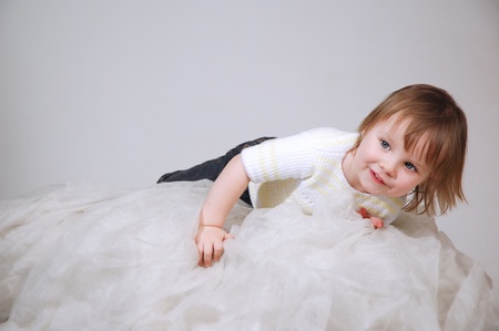 The nice little girl lying on a light fabric in studio and looking asideの写真素材