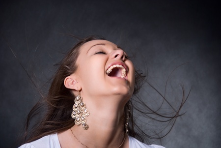 The young, beautiful girl with a flying hair, an open mouth and on a gray backgroundの写真素材