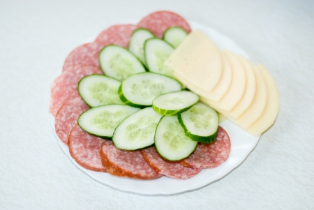 Cut cheese, sausage and cucumber in a plate on a tableの写真素材