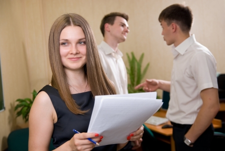 Portrait of sure young girl smiling with colleagues, discussing in a backgroundの写真素材