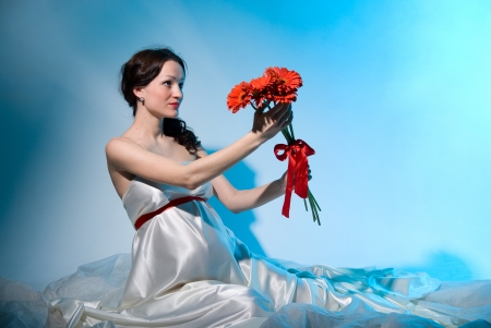 Pregnant woman holds flowers on outstretched arms on a blue backgroundの写真素材