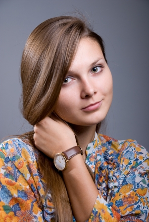 Portrait of a young beautiful girl with hand clock on a gray backgroundの写真素材