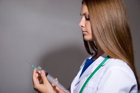 Young doctor with syringe on grey backgroundの写真素材