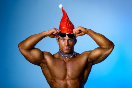 Strong athletic man in a cap of Santa Claus. Blue backgroundの写真素材