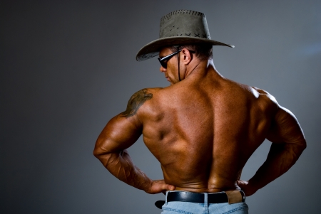 Muscular man in a cowboy hat and sunglasses on a gray backgroundの写真素材