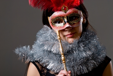 Close-up portrait of a girl in a mask with red feathers and tinsel. On a gray backgroundの写真素材
