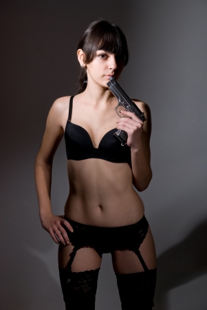 Sexy girl holding a black gun. on dark backgroundの写真素材