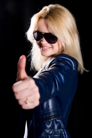 Young modern girl with thumb up against a black background.の写真素材