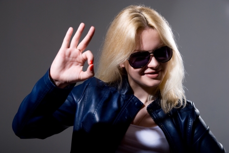 Girl in leather jacket and sunglasses showing "OK" gesture on a dark backgroundの写真素材