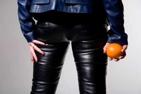 The girl in black leather pants with an orange in his hand. horizontal photoの写真素材