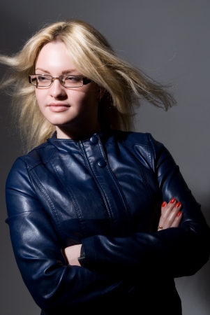 Portrait of a beautiful blonde in a cute leather jacket on a gray background. Looks asideの写真素材