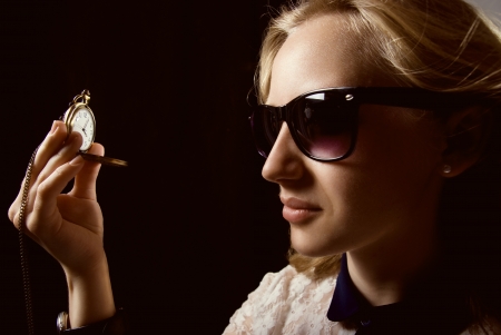 The girl in dark glasses holding a watch on a chain. On a black background in shades of yellowの写真素材
