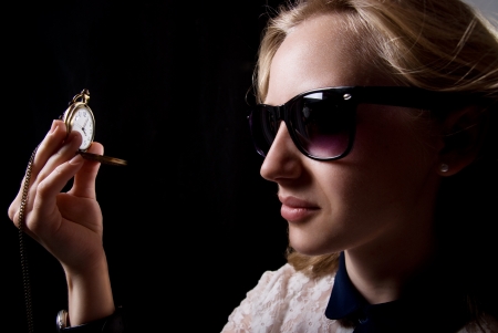 The girl in dark glasses holding a watch on a chain. On a black backgroundの写真素材