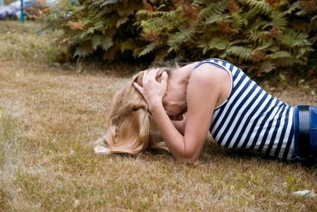 Girl lying on the grass and brown hands clutching his head. The girl problemsの写真素材