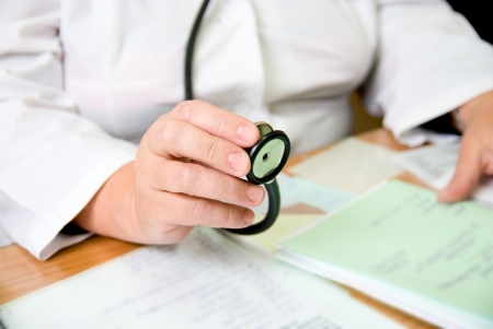 The doctor sits at a table holding a stethoscope in her hand. On the table are written notebooksの写真素材