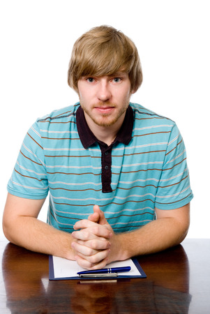 A young man is sitting at a desk. Looking at the camera isolated on a white backgroundの写真素材