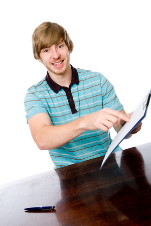 The young man points a finger at a blank sheet of sitting at the table. Isolated on white backgroundの写真素材