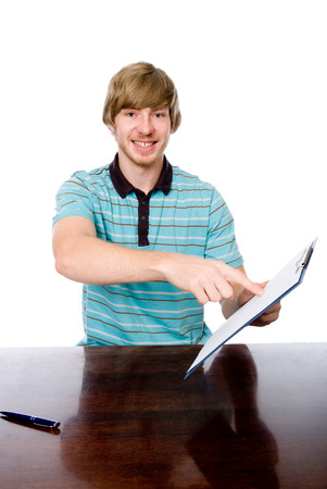 The young man points a finger at a blank sheet of sitting at the table. Isolated on white backgroundの写真素材