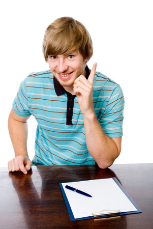 Portrait of a cheerful young man with a raised finger sitting behind a desk. isolated on white backgroundの写真素材