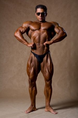 Bodybuilder flexing his muscles in studio. On a beige background athlete with sunglasses の写真素材