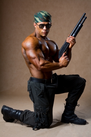 A muscular man with a gun. The guy in the soldiers' boots standing on one kneeの写真素材
