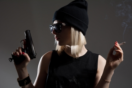 Beautiful girl with a gun in his hand and smoking a cigarette  Blonde in a dark hat in anticipation of an enemy spyの写真素材