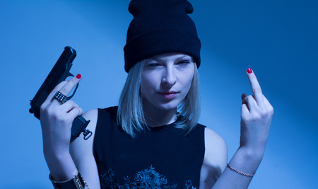 Angry young woman with a gun making obscene finger gesture.の写真素材