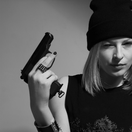 Young girl in a dark cap with a raised gun. Blonde with a gun. monochrome imageの写真素材