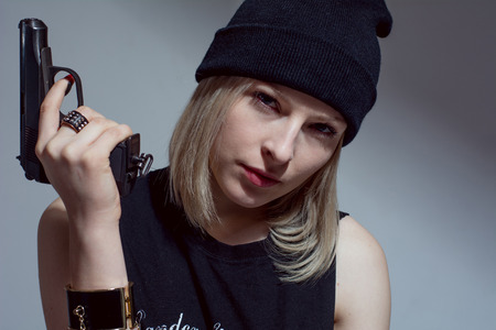 Young girl in a dark cap with a raised gun. Blonde with a gunの写真素材