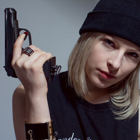 Young girl in a dark cap with a gun in his hand. Blonde with armsの写真素材