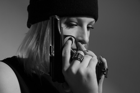 Young girl in a dark cap with a gun in his hand. Blonde with a gun. monochrome imageの写真素材