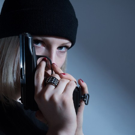 Young girl in a dark cap with a gun in his hand. Blonde with armsの写真素材