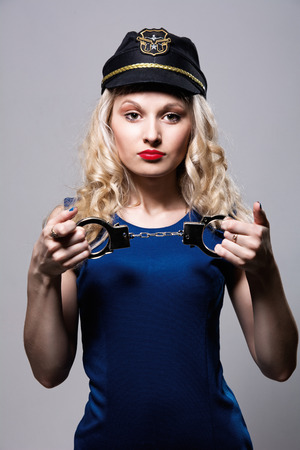 Beautiful girl with handcuffs and a police cap. Isolated on gray backgroundの写真素材