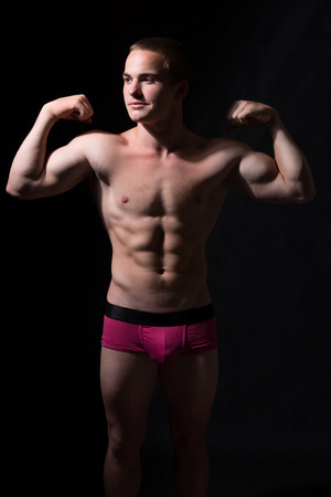 Muscular guy shows biceps. Sportsman smiling on a dark background and looking awayの写真素材