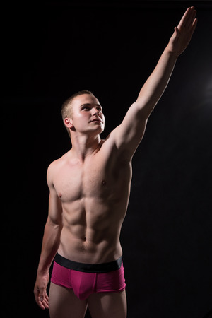 Young sportsman with a bare torso pointing towards isolated on a black backgroundの写真素材