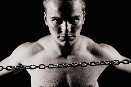 Close-up portrait of a young muscular guy with a metal chain. Isolated on a black backgroundの写真素材