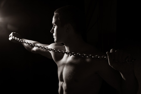 Portrait of a young muscular guy with a tight chain. Isolated on a black backgroundの写真素材