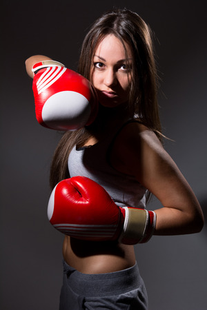 Beautiful girl with the boxing gloves,dark background. Upright posture to attackの写真素材