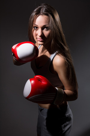 Beautiful girl with the boxing gloves,dark background. Upright posture to attackの写真素材
