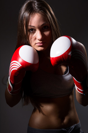 Young beautiful girl with the boxing gloves,dark background.の写真素材