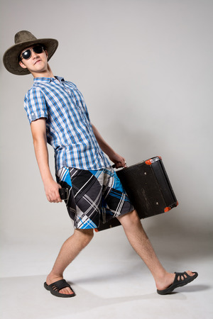 Portrait of a cheerful young guy tourist. A man with a suitcase going dark glasses and a hatの写真素材