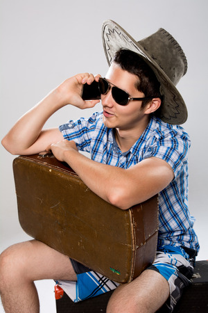 Man with suitcase talking on phone. A young man wearing a hat and sunglassesの写真素材